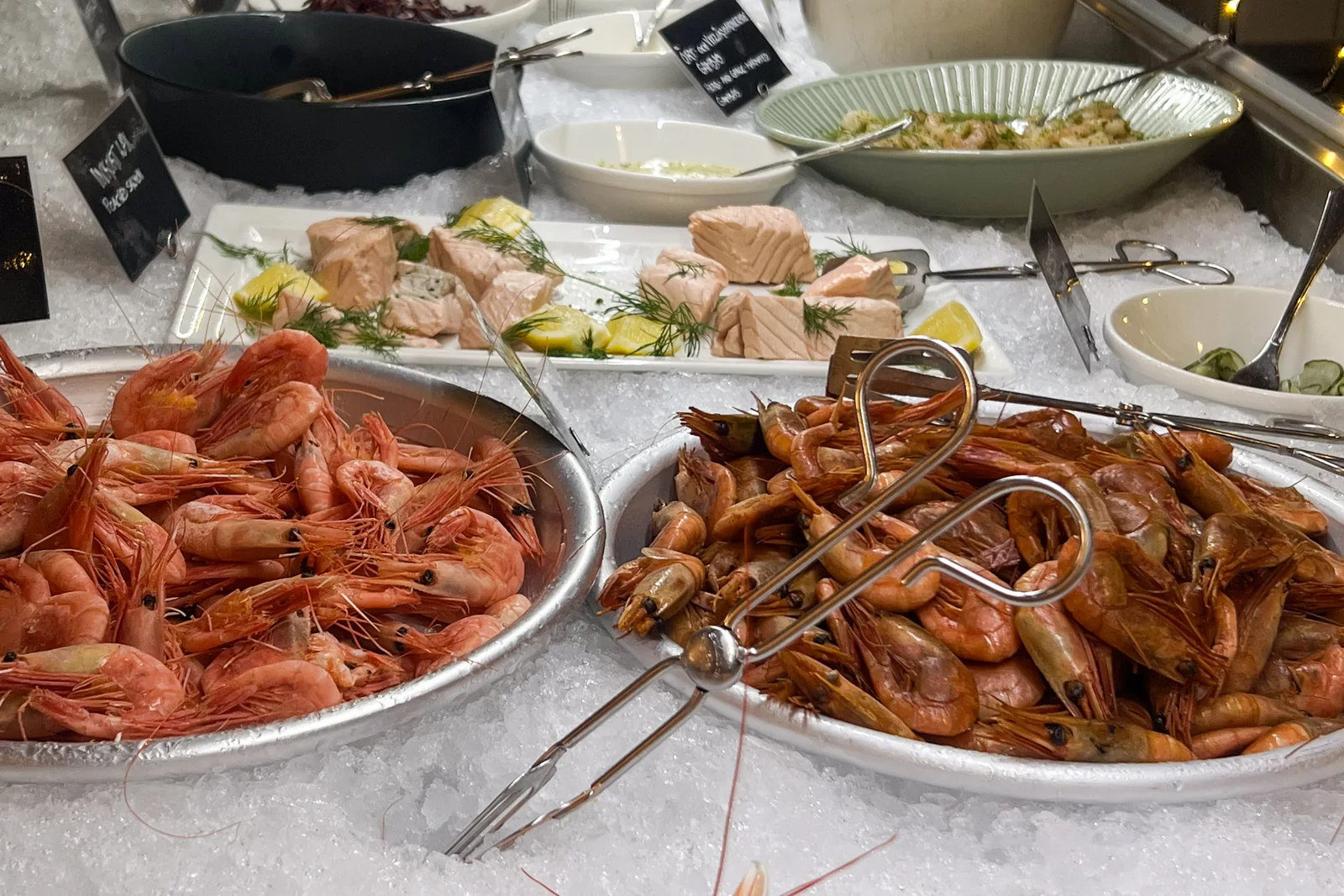 Två fat med räkor på is, lax med dill och citron bakom, och krittavlor vid faten