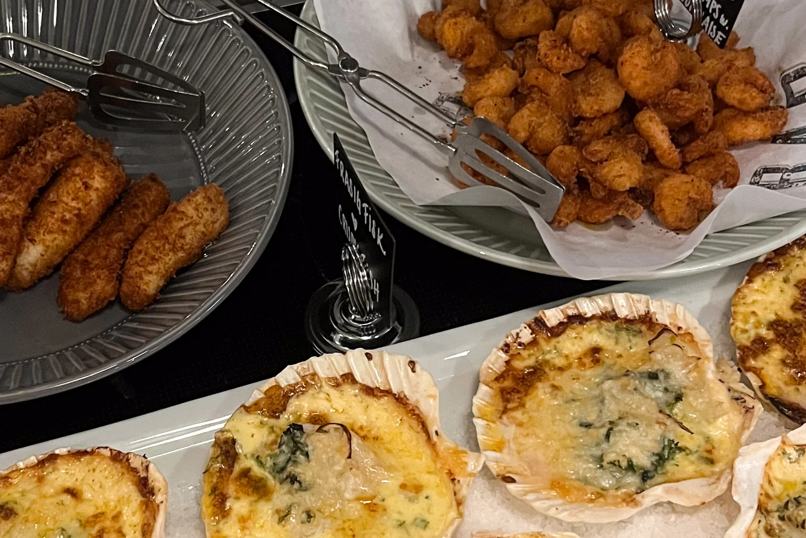 Panerade kroketter, friterade bitar i en skål och gratinerade musselskal på ett fat