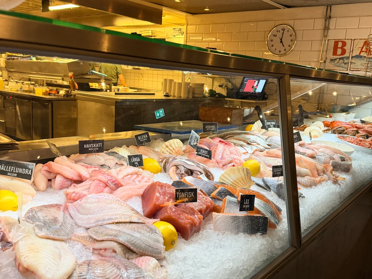 Fiskdisken i saluhallen, märkta fisksorter på is under en klocka på det vita kaklet
