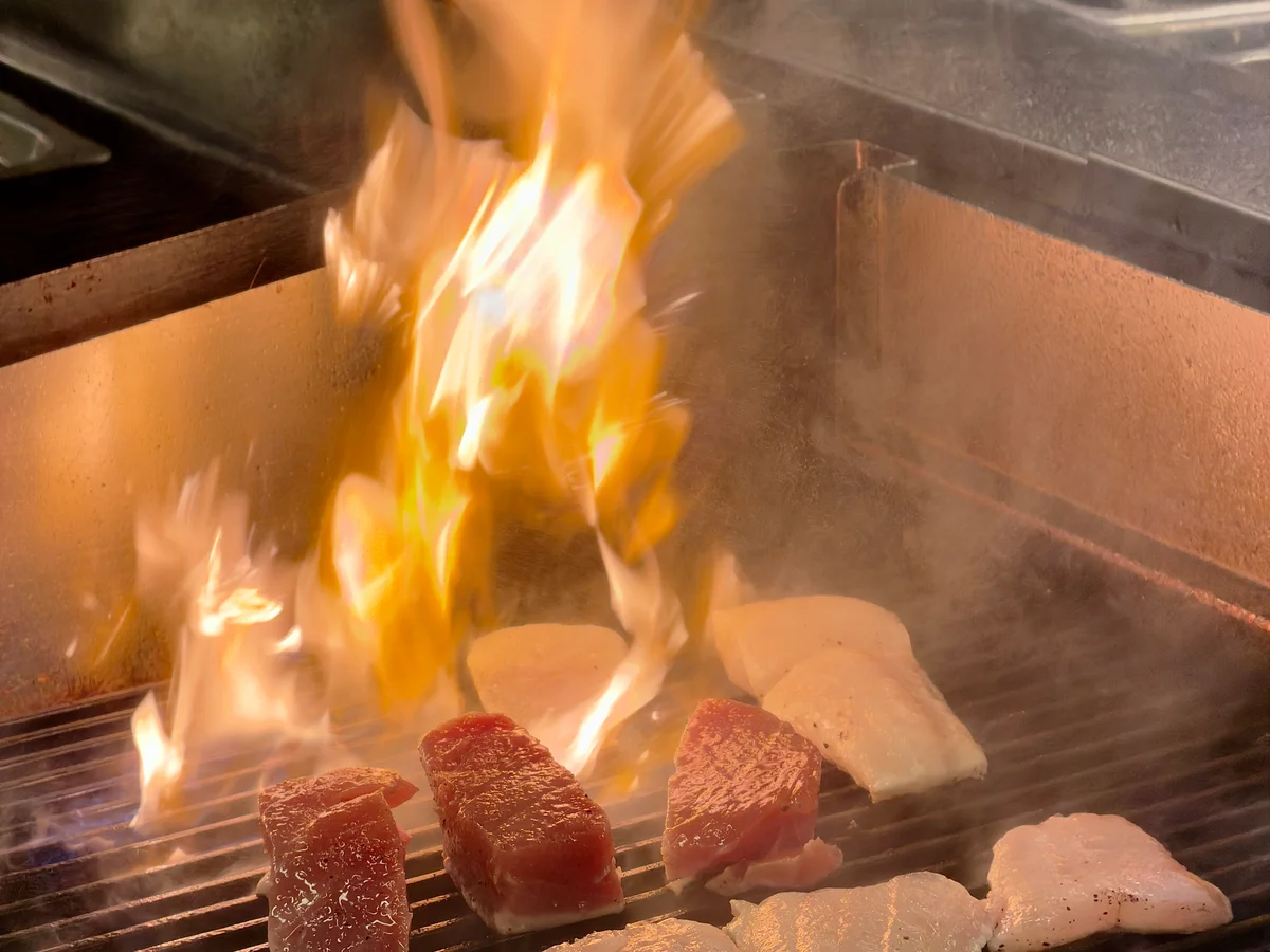 Tonfisk och annan fisk på den öppna grillen, med höga lågor